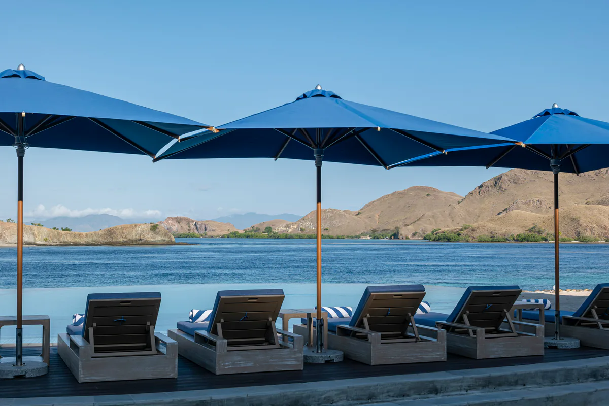 Sun loungers and umbrellas on the deck of the beachfront swimming pool at Komodo Resort