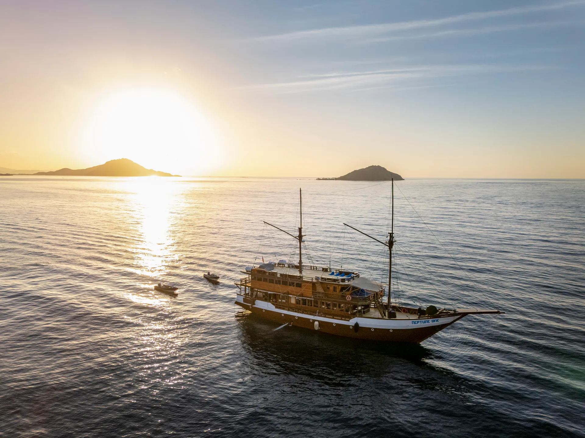 Neptune One phinisi liveaboard at sunset near an island